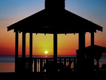 Silhouette built structure by sea against orange sky