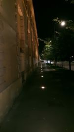 Illuminated street amidst buildings against sky at night