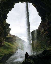 Rear view of woman standing against waterfall