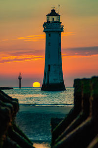 Lighthouse by sea against sky during sunset