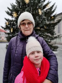Portrait of senior woman standing with granddaughter against christmas tree