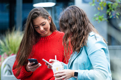 Two girlfriends use a smartphone, laugh and talk, technology concept with always connected milenials