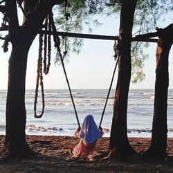 Rear view of woman on tree trunk by sea