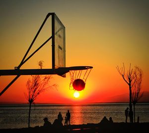 Silhouette basketball in hoop at beach against clear orange sky