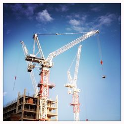 Low angle view of cranes at construction site against blue sky