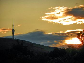 Silhouette of communications tower against cloudy sky