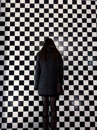 Rear view of woman standing against checked pattern wall