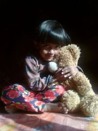 Portrait of girl holding teddy bear while sitting on bed at home