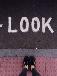 Low section of woman standing at sidewalk in front of look text on road