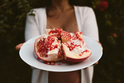 Woman hands holding dish with fresh pomegranate harvested from tree in the background red seeds