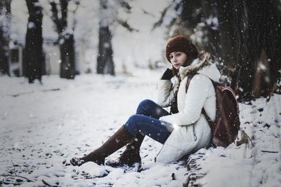 Portrait of woman sitting on snow covered field against trees