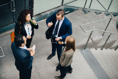 High angle view of business colleagues standing with food and drink at staircase in city