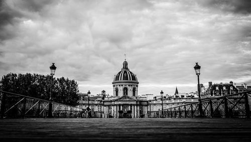 Pont des arts leading towards institut de france against cloudy sky