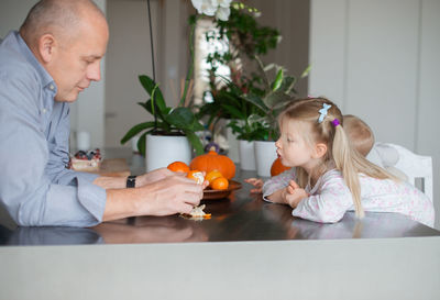 Grandfather giving orange fruit to children at home