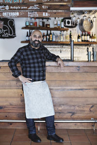 Full length of confident bartender standing by bar counter