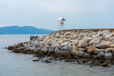 Lighthouse on rock by sea against sky