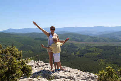 Fearless woman with adorable happy boy stand on steep edge of limestone plateau overlooking valley