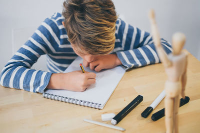 Boy drawing while sitting by table against wall