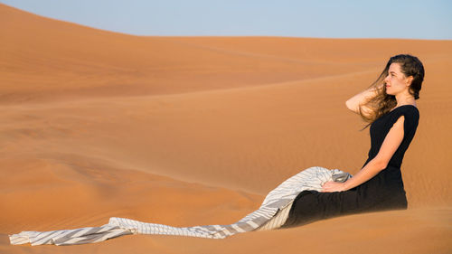 Woman sitting on sand dune at desert