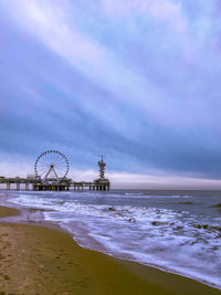 Ferris wheel at beach against cloudy sky