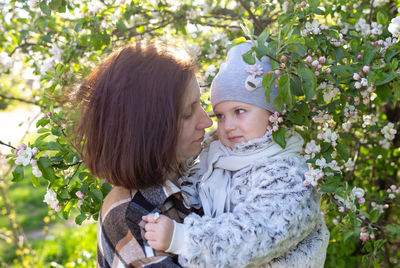 Young woman with her daughter in nature admires white flowering of spring trees