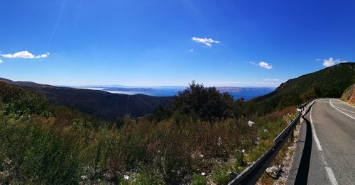 Panoramic view of road by mountains against blue sky