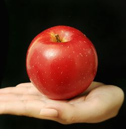 Cropped image of person holding apple against black background