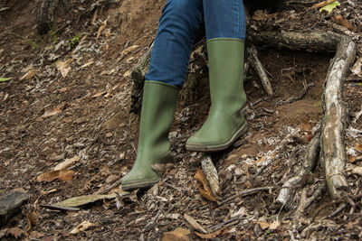 Low section of person with rubber boots sitting on ground in forest