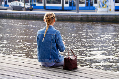 Rear view of woman sitting on pier over lake
