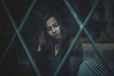Portrait of young woman looking through chainlink fence