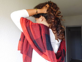 Rear view of woman tying her brown curly hair while at home
