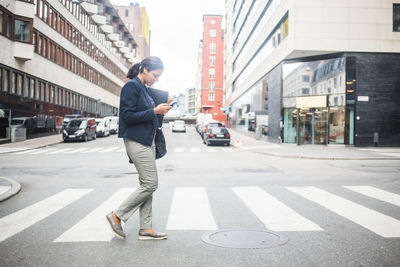 Businesswoman using mobile phone while crossing road
