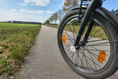 Bicycle on road amidst field against sky