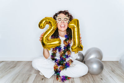 Young woman wearing mask sitting against wall at home