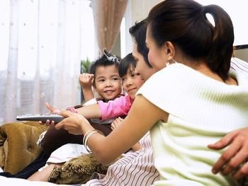 Side view of family holding remote control on sofa at home