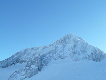 Low angle view of snow mountains against clear blue sky