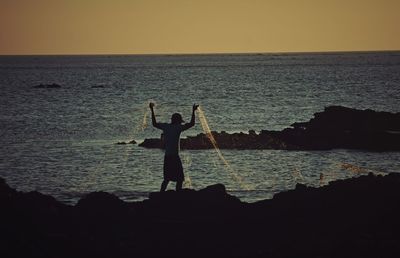 Silhouette man standing on beach against clear sky during sunset