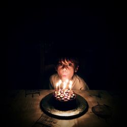 Young boy  illuminated  by birthday cake candles in a dark room