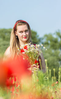 Portrait of young woman with red flower in field