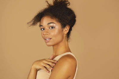 Portrait of young woman standing against yellow background