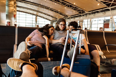 Family looking at mobile phone while sitting on chairs at airport terminal