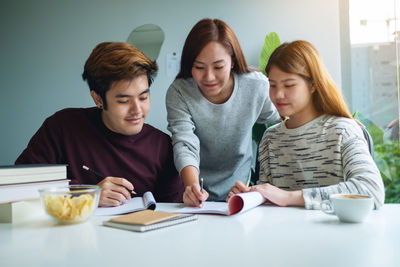 Group of young students tutoring and catching up workbook with friends