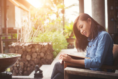 Side view of smiling woman reading book while sitting at yard