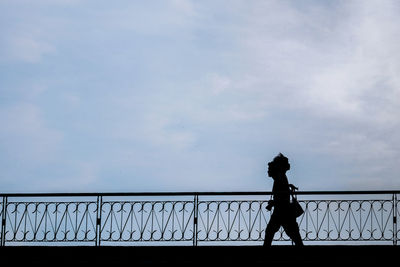 Silhouette man walking on bridge against sky