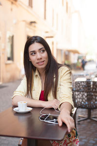 Thoughtful woman looking away while having coffee at sidewalk cafe