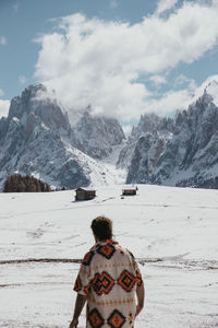 Rear view of man walking in snow and iverlooking snowy mountains