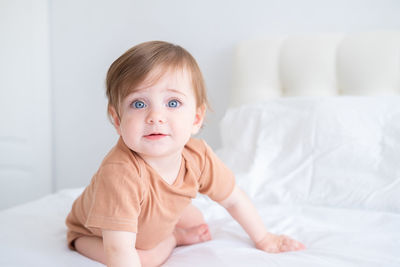 Portrait of cute baby girl sitting on bed at home