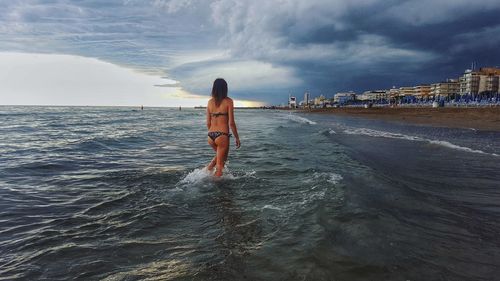 Rear view of woman standing on beach against sky