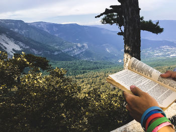 Midsection of person reading book against mountains