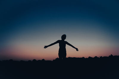Silhouette woman with arms outstretched standing against sky during sunset